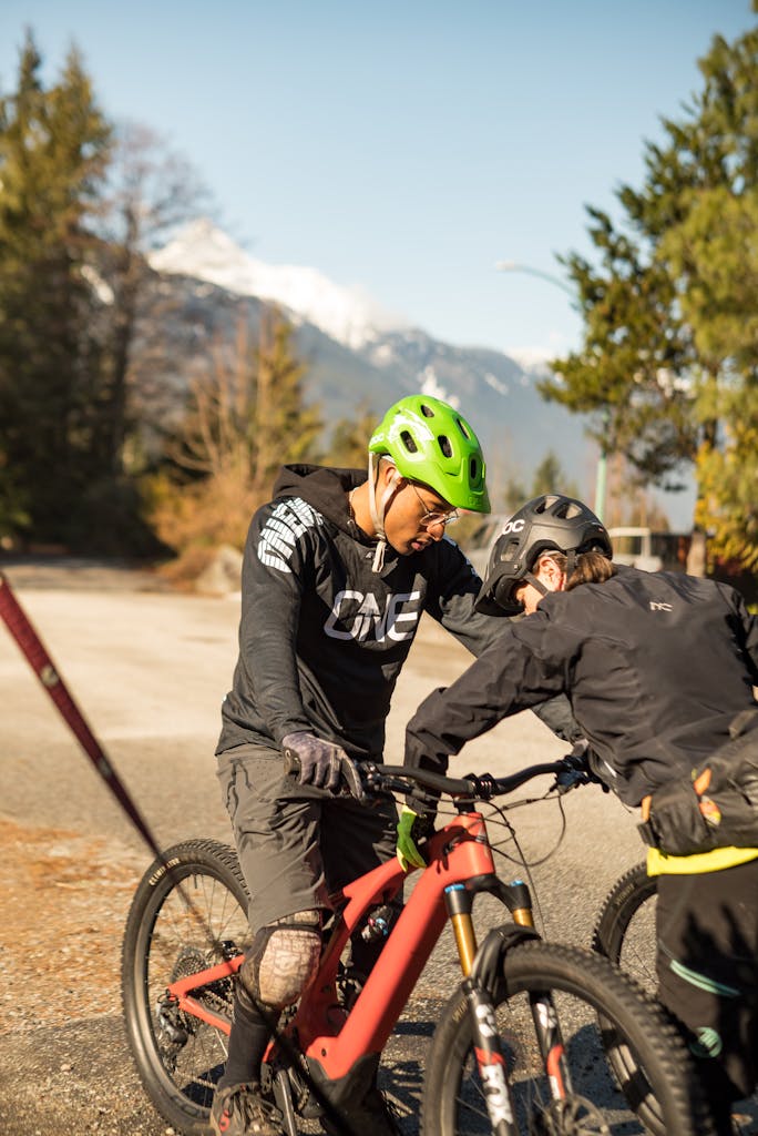 Two cyclists in protective gear prepare for a mountain bike adventure in a scenic countryside setting.